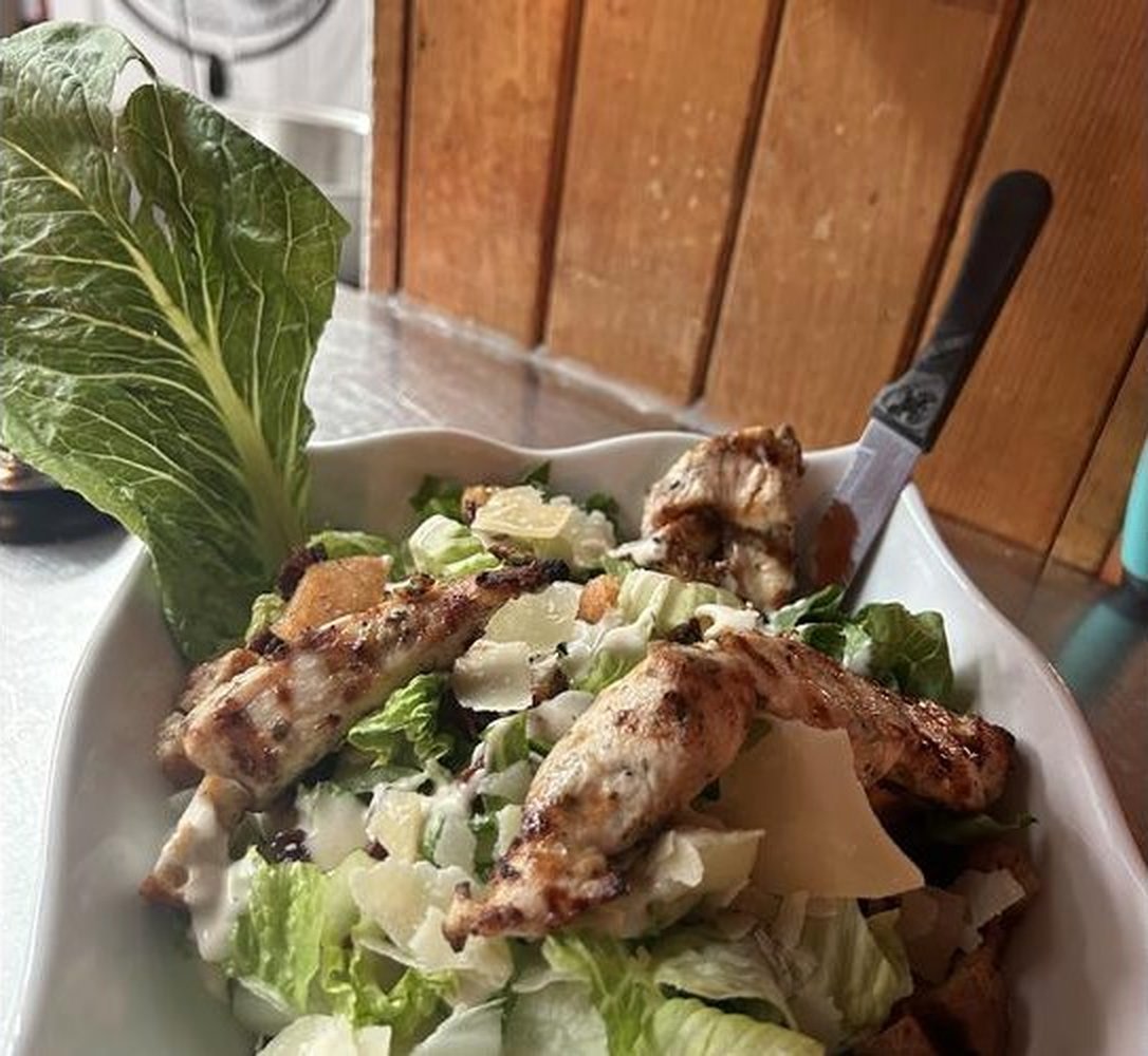Une salade César au poulet grillé, copeaux de parmesan et croûtons maison